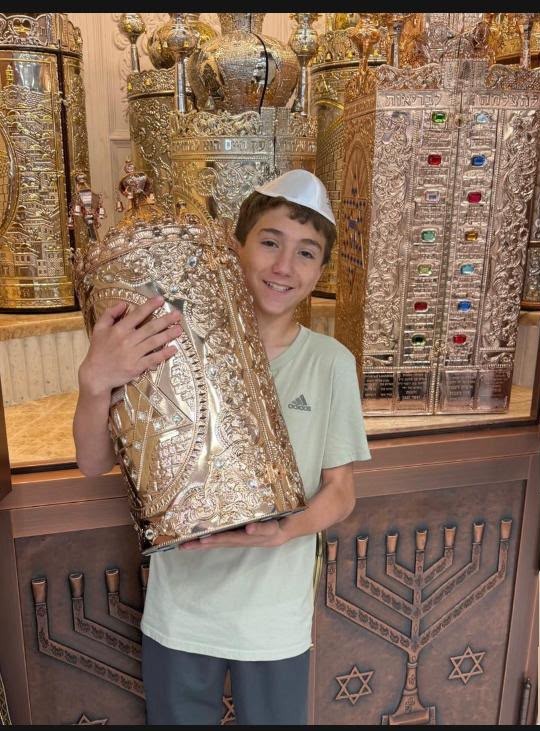 Dan Levanon smiling while holding a Torah scroll in a decorated silver case